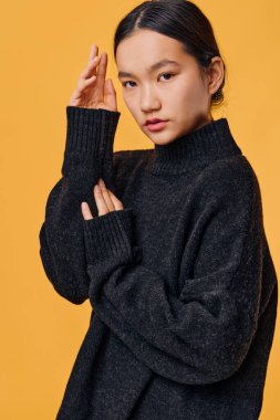 Saf turuncu arka planda duran, siyah saçlı, kalın kazaklı bir manken. Düşünceli ifadeyi ve sonbahar sezonu için çağdaş modayı gösteren sıradan bir portre.