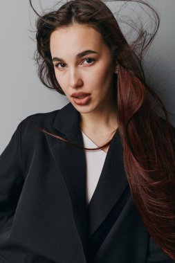 Siyah kıyafetli, dalgalı kahverengi saçlı ve az makyajlı bir kadın kameraya bakıyor. Stüdyoda sıradan saç stili ve tarafsız yüzlü kadın modelin yakın plan portresi..