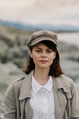 Dokulu ceketli genç bir kadın portresi ve açık hava gazeteci şapkası ve bulanık doğa geçmişi. Gündelik moda, sonbahar tarzı ve kendine güvenen kadın modeli..