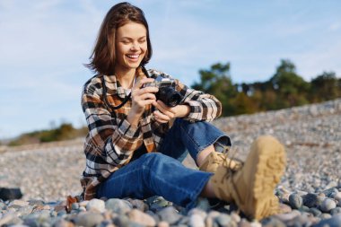 Fotoğrafçı kadın plaj kamerası gelişigüzel objektifi, kayalık bir sahilde doğal ışık, neşe, odak ve yaratıcı açık hava fotoğrafçılığı ile samimi bir anı yakalıyor..