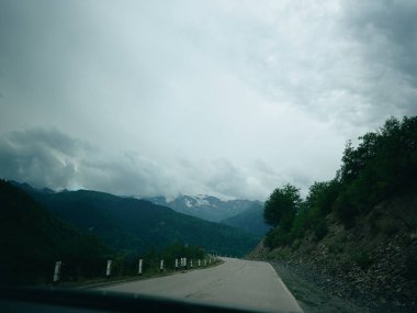 Bulutlu vadi yolu Alp arazisi, kayalık kıyılar ve sık ağaçlar, sessiz seyahat sahneleri, kasvetli gökyüzü ve uzak kar örtüleri, davetkar yolculukları ve açık hava keşifleri