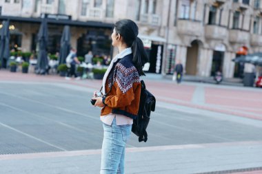 Kadın, sokak, sırt çantası, kentsel, gündelik, moda, ceket, kot, kamera, güneşli bir kare içinde seyahat yaşam tarzı, moda belirleme kıyafeti, sokak modası ve modern şehir atmosferi