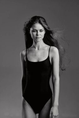 Siyah ve beyaz bir kadın portresi siyah bir beden giyiyor, saçları akıyor ve yüzünde düz bir arkaplan karşısında sakin bir ifade var. Kavram: minimalizm ve zarafet