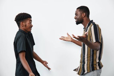 Esmer tenli Afro-Amerikalı erkekler çizgili ve siyah gömleklerle konuşuyorlar. Genç siyah erkekler beyaz arka planda etkileyici vücut diliyle aktif olarak iletişim kuruyorlar..