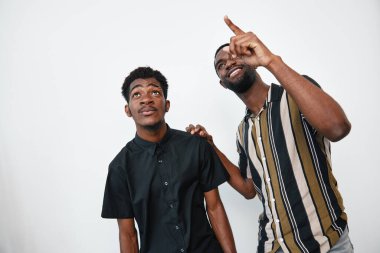 Siyah tenli Afro-Amerikalı erkekler beyaz arka planda poz veriyorlar. Biri yukarı bakıyor, diğeri ise stüdyoda dostluk ve rahatlama havası gösteriyor..