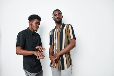 Siyah tenli iki Afrikalı Amerikalı adamın portresi. Günlük giysiler giyiyorlar. Beyaz, pürüzsüz arka planda farklı yüz ifadeleri sergiliyorlar..
