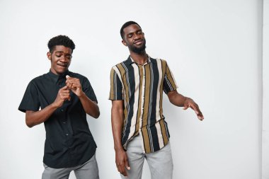 Esmer tenli Afro-Amerikalı erkekler çizgili ve siyah tişörtlerle beyaz stüdyo geçmişine karşı dans ederek eğleniyorlar..