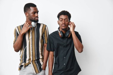 Siyah tenli, sıradan kıyafetler ve kulaklıklı Afro-Amerikalı erkekler beyaz arka planda poz veriyorlar. Genç arkadaşlar, müzik severler ve modern şehir modası ve bağlantısı olan yaşam tarzı.