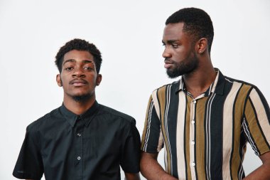 Esmer tenli, sıradan gömlekler giyen iki Afro-Amerikalı adamın portresi. Bir adam tarafsız bir ifadeyle öne bakıyor, diğeri ise beyaz arkaplanda düşünceli bir poz veriyor..