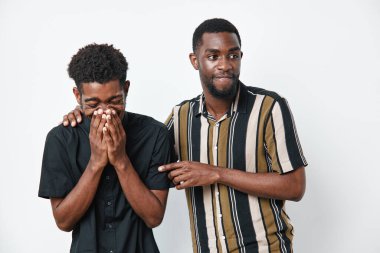 Esmer tenli Afro-Amerikalı erkekler günlük kıyafetlerle gülüp eğleniyorlar. Arkadaşlık, neşe ve rahat bir atmosfer. Beyaz arka planda eğlenceli etkileşimlerden hoşlanan iki genç erkek..