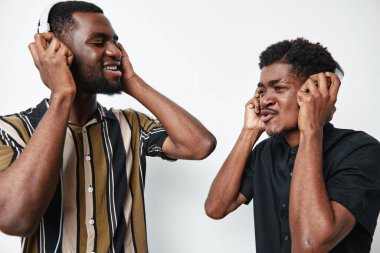 Koyu tenli genç adamlar kulaklıkla müzik dinliyorlar, neşe ve bağlantı belirtiyorlar, parlak stüdyoda çizgili ve sağlam desenleri olan günlük gömlekler giyiyorlar..