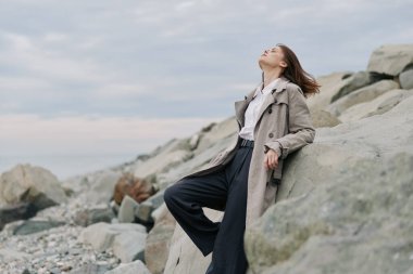 Gündelik giysiler içindeki kadın deniz kenarındaki kayalıklarda dinleniyor, kafası kapalı gözlerle arkaya eğilmiş. Sahil kenarında sakin, doğa, özgürlük ve barışçıl bir an..