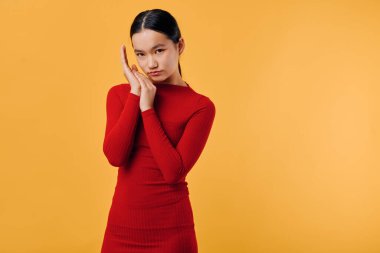 Kırmızı uzun kollu elbiseli bir kadın model kameraya bakıyor ve elleri başının yanında. Minimalist sarı zemin, zarif poz, moda fotoğrafçılığı, güzellik, kendine güvenen ruh hali ve modern tarz konsepti..