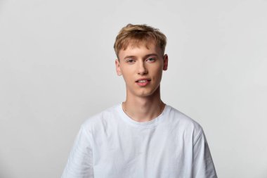 Beyaz tişörtlü genç adam basit bir stüdyoda duruyor, sakin duruş ve temiz estetik moda, yaşam tarzı, reklamcılık ve yaratıcı kavramlar için ideal.