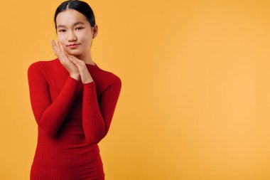Dar kırmızı bluzlu gülümseyen Asyalı kadın turuncu arka planda duruyor. Temiz tenli, rahat moda veya yaşam tarzı konsepti için poz veren kendinden emin bir kadının stüdyo fotoğrafı..