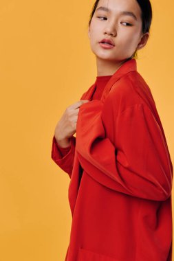 Kırmızı ceketli genç bir kadın, sarı arka fona karşı duruyor, tasmasını tutuyor, başka tarafa bakıyor, şık moda konsepti, canlı kıyafetler, temiz arka planda çekilmiş kapalı bir fotoğraf çekimi..