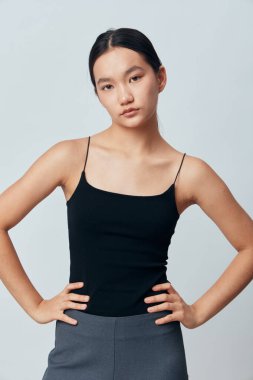 Siyah kolsuz bluzlu ve gri pantolonlu kendine güvenen kadın modelleri, elleri kalçalarında, ciddi ifadelerinde ve arka planda rahat bir duruş sergilerler..