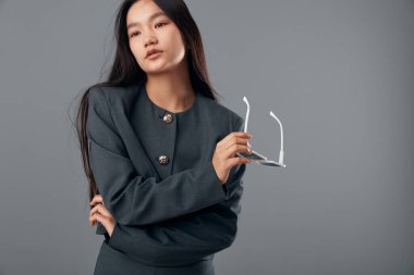 Uzun saçlı, gri ceketli ve gözlüklü profesyonel bir kadının portresi. Kapalı alanda kollarını bağlayan ciddi düşünceli bir yüz ifadesi..