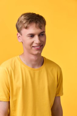 Parlak bir stüdyo arkaplanına karşı sarı tişörtlü gülümseyen adam gündelik tarzını, yaklaşılabilir havasını, temiz kompozisyonunu ve günlük moda estetiğini aktarıyor.