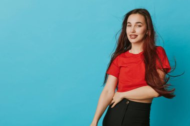 Kırmızı bluzlu ve siyah pantolonlu gülümseyen kadın manken rahat duruşu ve bol saçı olan, moda, güzellik ve yaşam tarzı konsepti için mavi arka planda duruyor..