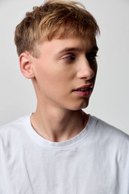 Beyaz tişörtlü genç bir erkeğin yan profili, ince stüdyo gölgeleri, doğal duruş, çağdaş moda atmosferi, minimal stil, yaklaşımlı ve düşünceli ruh hali, taze ve basit estetik