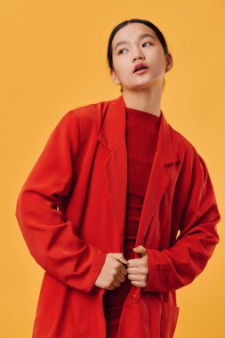 Kırmızı ceket ve süveter giymiş doğal makyajlı manken stüdyoda parlak sarı arka plana karşı duruyor, sakin ve kendine güvenen bir tutum takınıyor..