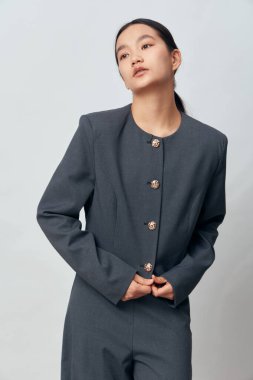 Koyu gri takım elbise giyen profesyonel bir kadın model beyaz arka planda yalnız poz veriyor ciddi yüz ve eller moda ya da iş konsepti için ceket tutuyor..