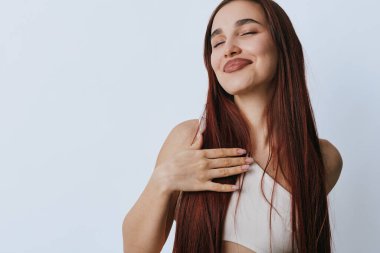 Uzun kahverengi saçlı, eli göğsünde, gözleri kapalı genç bir kadın minnettarlığını gösteriyor. Huzurlu yüz ve rahat duruş sade ışık arka planda sağIık için.