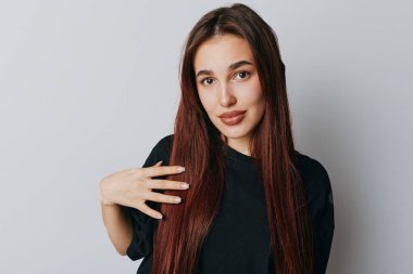 Uzun kahverengi saçlı, siyah bluzlu, elleri göğsünde poz veren kendine güvenen genç bir kadının portresi. Yumuşak ışıklandırma ve basit arkaplan ile stüdyo çekimi.