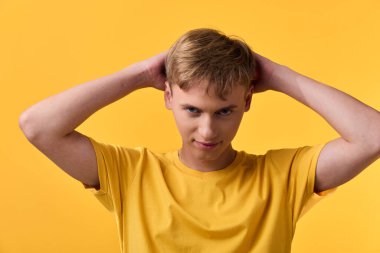 Elleri başlarının üzerinde sarı tişörtler giyen genç, kendine güvenen bir duruş ve rahat bir ruh hali, kalın renkte temiz bir stüdyo tarzı.