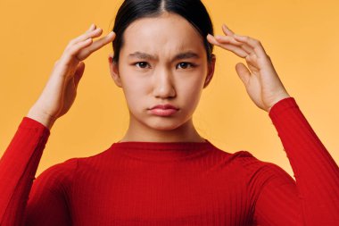 Alnına kırmızı uzun kollu tişört giyen, çatık kaşlı ve gergin yüzlü parlak turuncu arka planda duran üzgün kadının portresi..