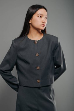 Detaylı düğmeleri olan şık gri ceketli Asyalı kadın portresi. Moda konsepti için minimal stüdyo ortamında kendinden emin duran bir kadın model..