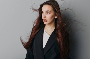 Siyah ceketli, beyaz gömlekli, kahverengi saçlı, kendinden emin genç bir kadının portresi. Yumuşak ışıklandırmalı, minimalist gri arkaplan model ya da yaşam tarzı için doğal görünüş ve gündelik tarzı vurguluyor.