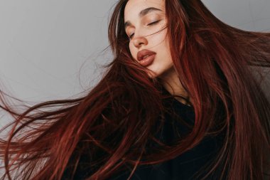 Canlı kızıl saçlı ve siyah elbiseli sakin yüzlü genç bir kadının portresi. Güzellik fotoğrafçılığında zarif ve tarz sahibi olmak için hafif ışıklandırma ve saç üfleme ile stüdyo çekimi.