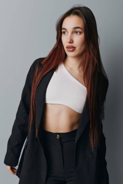 Siyah ceketli, beyaz bluzlu, rahat duruşu olan, kameradan uzağa bakan, uzun düz saçlı genç bir manken..