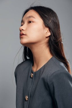 Gri zarif ceketli genç bayan model moda portresi için yan poz veriyor. Profesyonel stüdyo ortamında temiz makyaj ve uzun saç..