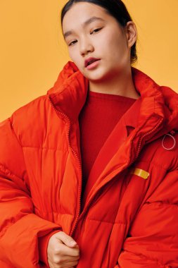 Kadın modelin portresi fermuarlı parlak kırmızı yastıklı ceket giyiyor, elleri elbisenin üstünde duruyor, sıcak kıyafetler ve sarı arka planlı modern moda..