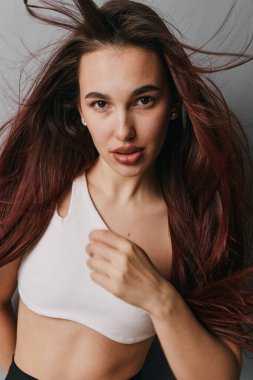 Beyaz ekin bluzlu, dalgalı saçlı, portre için poz veren kendinden emin genç bir kadın. Doğal görünüşü ve rahat duruşu olan, tarafsız arka planı olan bir kadın model..