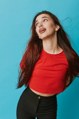 Kırmızı tişörtlü ve siyah pantolonlu genç kadın modelin portresi mavi arka planda duruyor. Moda tarzı için duygu ve modern günlük kıyafetleri gösteriyor..