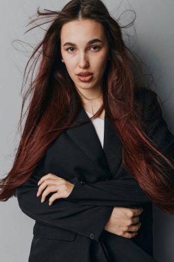 Siyah ceketli, kendinden emin, uzun saçlı, kollarını kavuşturmuş, minimalist stüdyo fotoğrafçılığına dik dik bakan genç bir manken..
