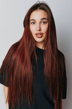 Uzun kızıl saçlı, siyah gömlekli ve sakin yüzlü kameraya bakan genç bir kadın portresi. Basit arka plan ve doğal güzellik ile stüdyo çekimi saç ve yüze odaklan.