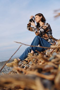 Sahil boyundaki düşünceli fotoğrafçı, açık bir gökyüzünün altında dalgaları, ufukları ve uzak kıyı şeritlerini vurmak için çimlerin ve kayaların üzerine diz çöküp gündelik kıyafetlerini giyen bir kamera kullanıyor..