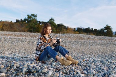 Kayalık sahilde sıradan bir kadın fotoğrafçı, bir kamera, kot ve bot, doğal ışık, seyahat veya hobi fotoğrafçılık için sakin manzara, açık hava keşfi ve rahatlama ile detayları yakalıyor..