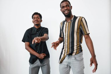 Siyah tenli Afro-Amerikalı erkekler günlük gömlekler giyip, kot pantolon giyip dans ediyor ve eğleniyorlar. Beyaz stüdyoda iki arkadaşla mutluluk, arkadaşlık ve yaşam tarzı konsepti.