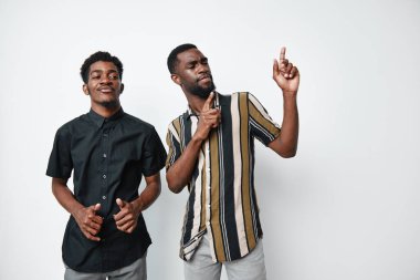 Siyah tenli, sıradan gömlekli Afrikalı erkekler beyaz arka planda birlikte poz veriyorlar. Gülümseyen yüzler, dostça bir jest ve kendine güvenen bir yaşam tarzı ve arkadaşlık..