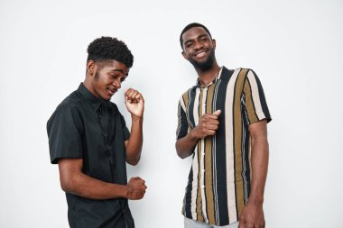 İki koyu tenli siyah adam, günlük gömlekler giyip beyaz arka planda gülümseyip dans ediyorlar. Stüdyo fotoğraflarında mutluluk, dostluk ve gençlik hayatı..