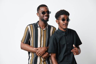 Gündelik giysiler ve güneş gözlükleriyle siyah tenli Afrikalı erkekler beyaz arka planda birlikte poz veriyorlar. Modern tarzda stüdyo fotoğraflarında kendinden emin ve mutlu görünüyorlar..