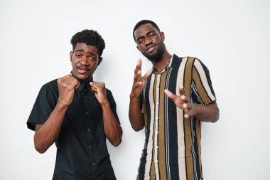 Siyah tenli Afrikalı erkekler beyaz arka planda duruyor. Biri siyah gömlekli, yumruklu, diğeri çizgili gömlekli. Etkileşim için el hareketlerini gösteriyor..