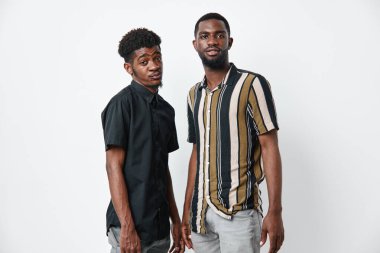 Siyah tenli, sıradan gömlekler giyen iki siyah adamın portresi. Afrika etnik köken, arkadaşlık, güven, modern moda ve beyaz arka plan ve rahat pozlarla stüdyo ortamları.