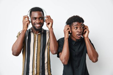 Siyah tenli genç adamlar kulaklıkla müzik dinliyorlar. Neşelerini ve şaşkınlıklarını dile getiriyorlar. Sıradan çizgili ve siyah gömlekler giyiyorlar..